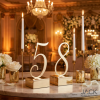 Gold calligraphy number standees side view grand ballroom candles florals warm ambient lighting