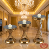 Gold 3-tier cake stand set ascending heights side view ballroom chandeliers marble floors spiral shadows