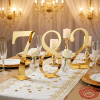 Gold script number standees at wedding reception table warm spotlights decorative accents 45 degree