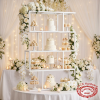 White multi-tier shelf at romantic all-white wedding dessert table flowers candles soft bokeh